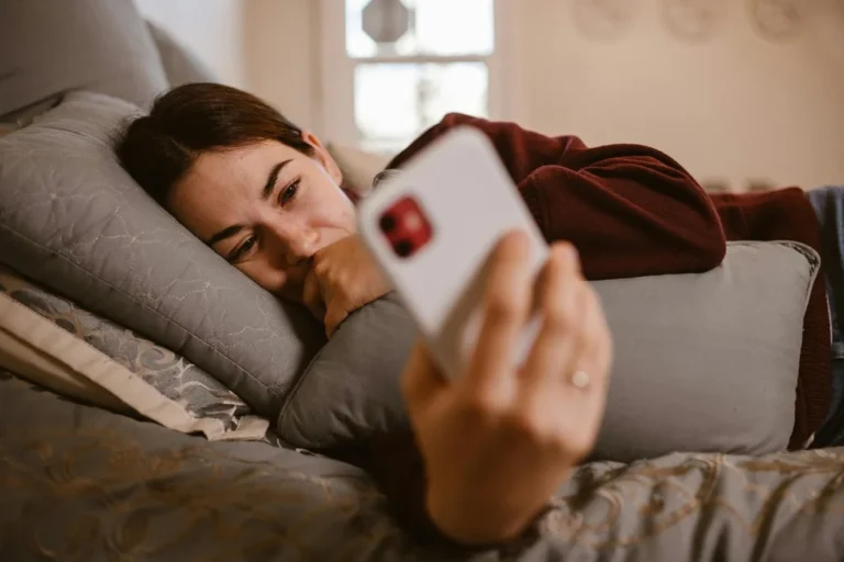 paní leží v posteli a kouká do mobilu